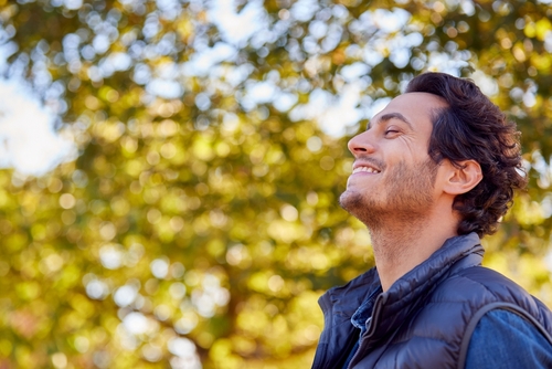 side of man outside with trees smiling with eyes closed looking happy
