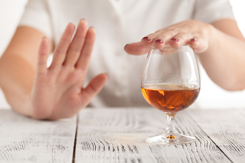 close up of glass of brandy with woman hand over the glass and her other hand signaling no