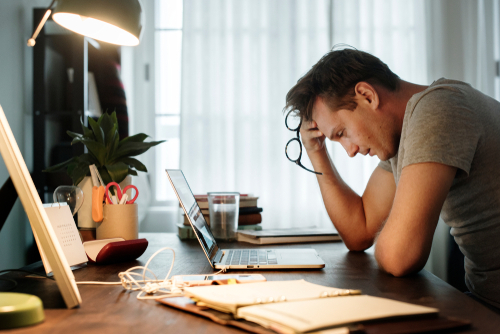man at desk with papers holding head looking stressed
